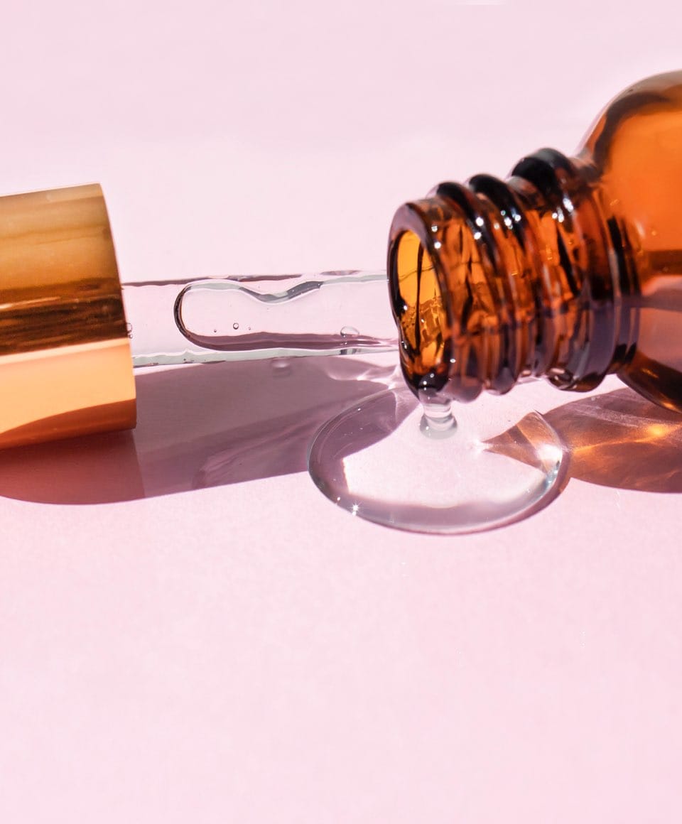 A glass dropper bottle made of brown glass against a pink background casts a shadow