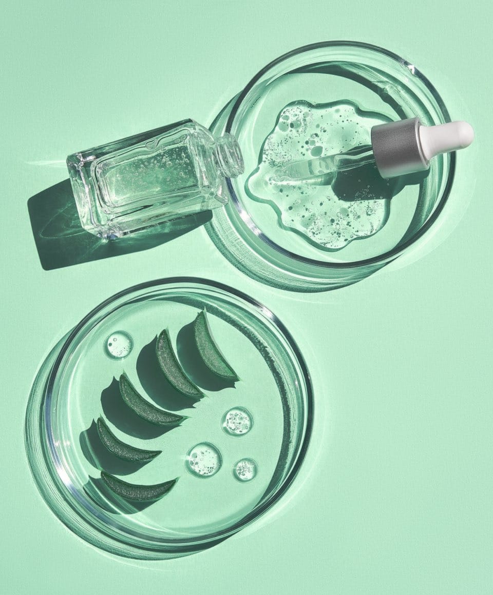 Flat lay of cosmetics serum and and laboratory glassware with fresh leaves of aloe vera on bright green background